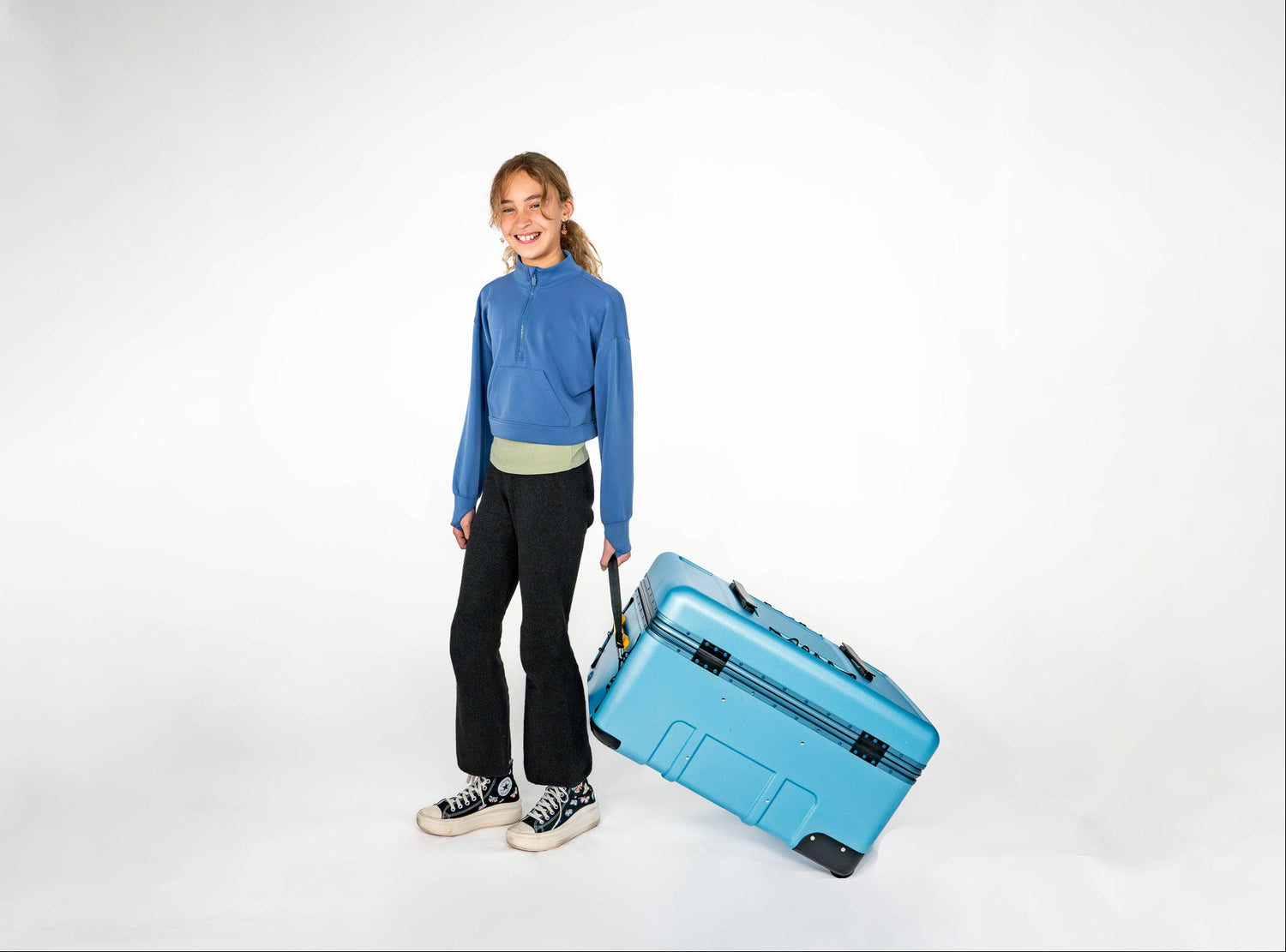 Smiling child pulling a blue Belonging LifeLocker Founders Bundle by the handle on a white studio background.