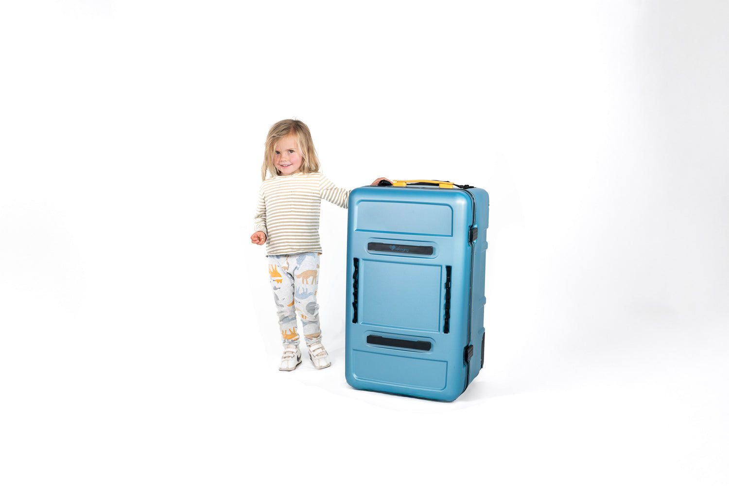 Young child standing next to a closed blue Belonging LifeLocker Founders Bundle, smiling and holding the handle on a white studio background.